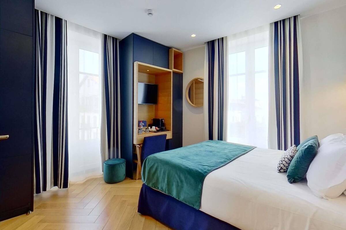 Une chambre d’hôtel comprenant un lit, un bureau, une chaise, un miroir rond et une armoire.