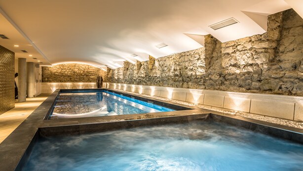 A spa area with a hot tub and a rectangular pool, stone walls, and a modern ceiling design.