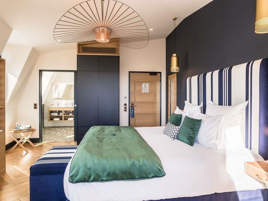 Ein modernes Schlafzimmer mit einem großen Bett, einer außergewöhnlichen Deckenleuchte und Blick auf einen Küchenbereich.