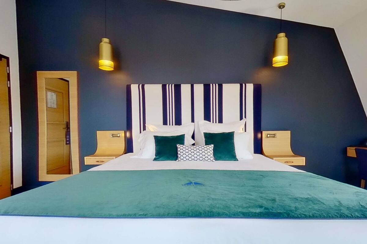 Ett modernt hotellrum med en stor säng, två sängbord, en sänggavel med vertikala ränder och två hängande lampor.