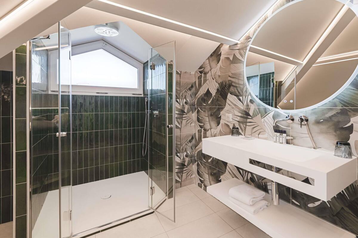 A modern bathroom with a glass-enclosed shower, a vanity with a mirror, and a wall with a leaf pattern.