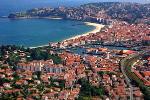 Vista aérea de una ciudad costera con edificios de techos rojos, una playa y un puerto deportivo.