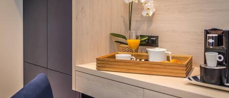 A modern hotel room with a wooden desk, a blue chair, a tray with a white mug, a glass of orange juice, and a white orchid.