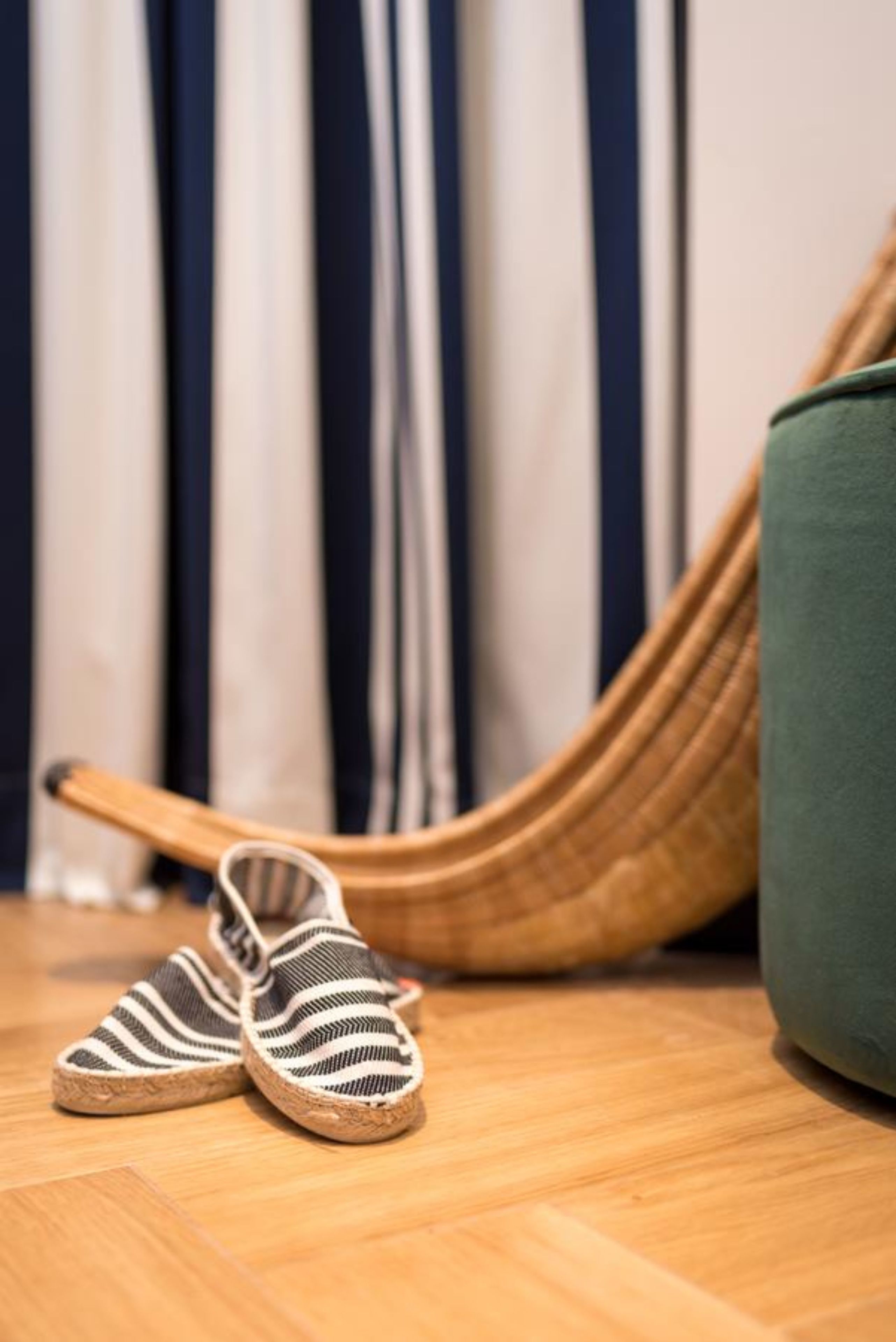 A pair of striped slippers on a wooden floor, a woven chair, and a green cushion.