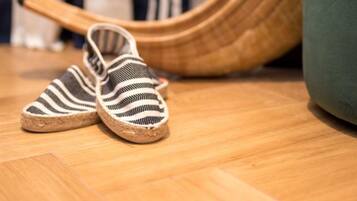 Streeppatroon slippers op een houten vloer, een geweven stoel en een groene kussen.
