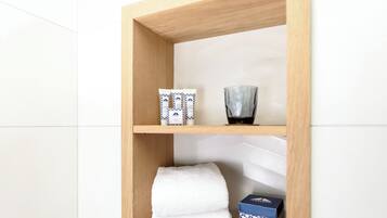 Un estante de madera con artículos de aseo, un recipiente de vidrio y una toalla doblada.