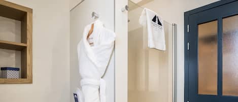 A bathroom with a glass shower door, a wooden shelf with a patterned box, and a white towel hanging on a hook.