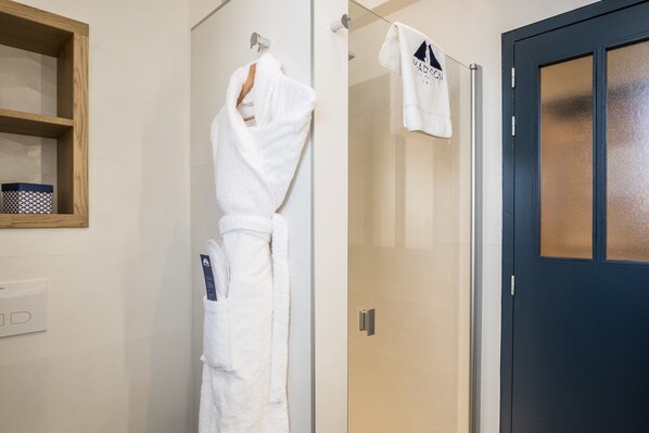 A bathroom with a glass shower door, a wooden shelf with a patterned box, and a white towel hanging on a hook.