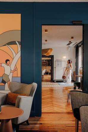Un intérieur moderne avec un parquet en bois disposé en chevrons, une grande peinture abstraite et une personne traversant un passage.
