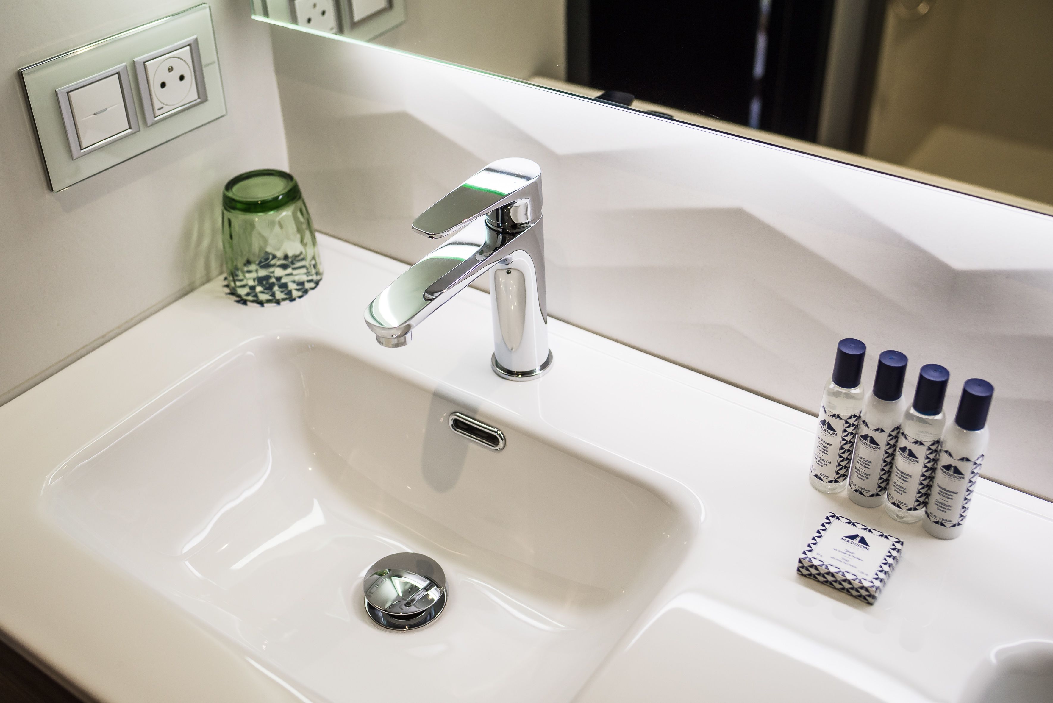 A white bathroom sink with a chrome faucet, a glass jar, and four bottles of toiletries.