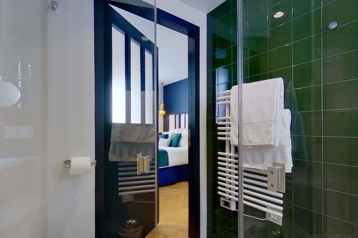 Ein modernes Badezimmer mit Duschkabine aus Glas, Toilette sowie ein sichtbarer Schlafbereich mit Bett und Nachttisch.