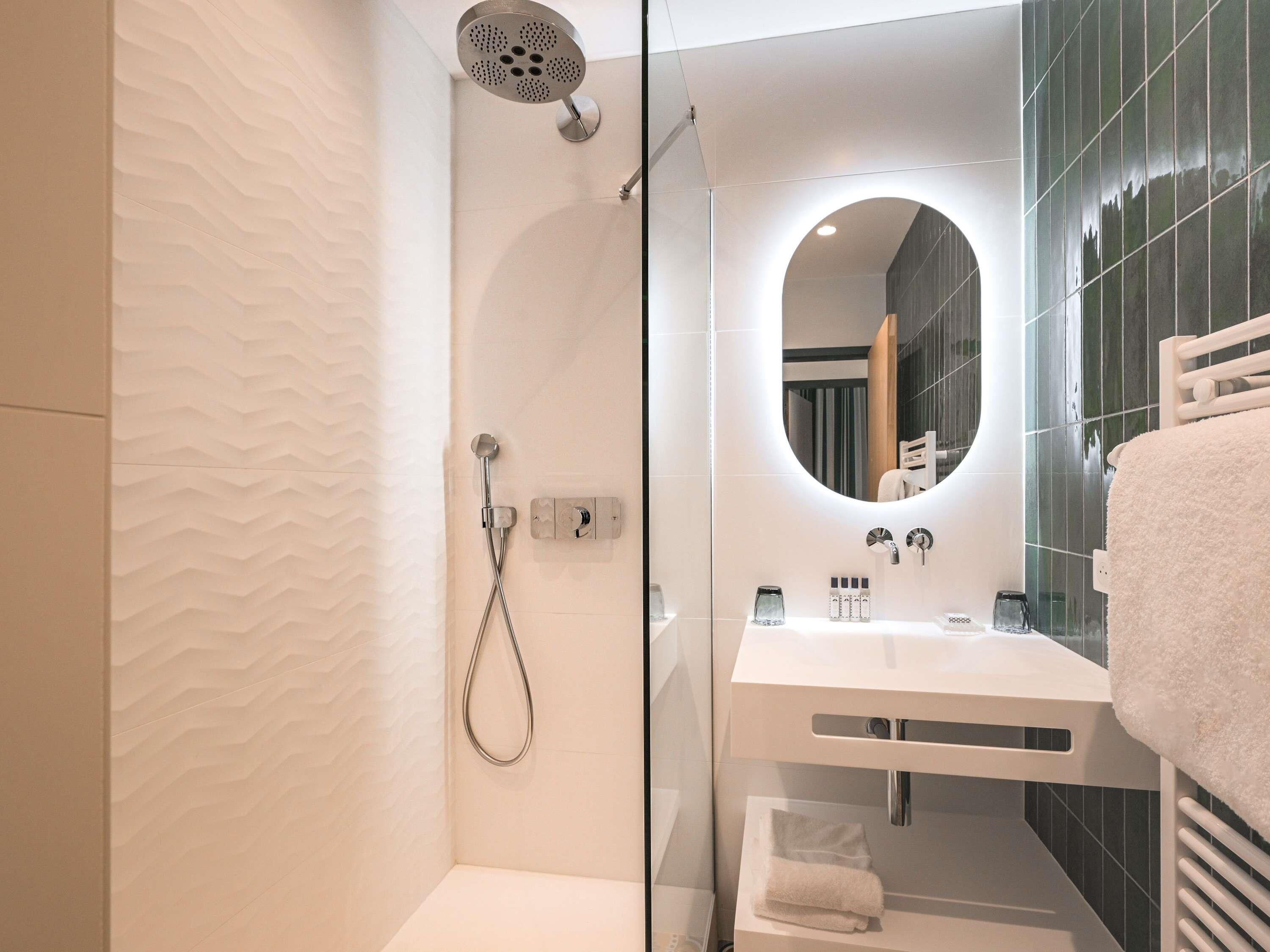A modern bathroom with a shower, a sink, a mirror, and a towel rack.