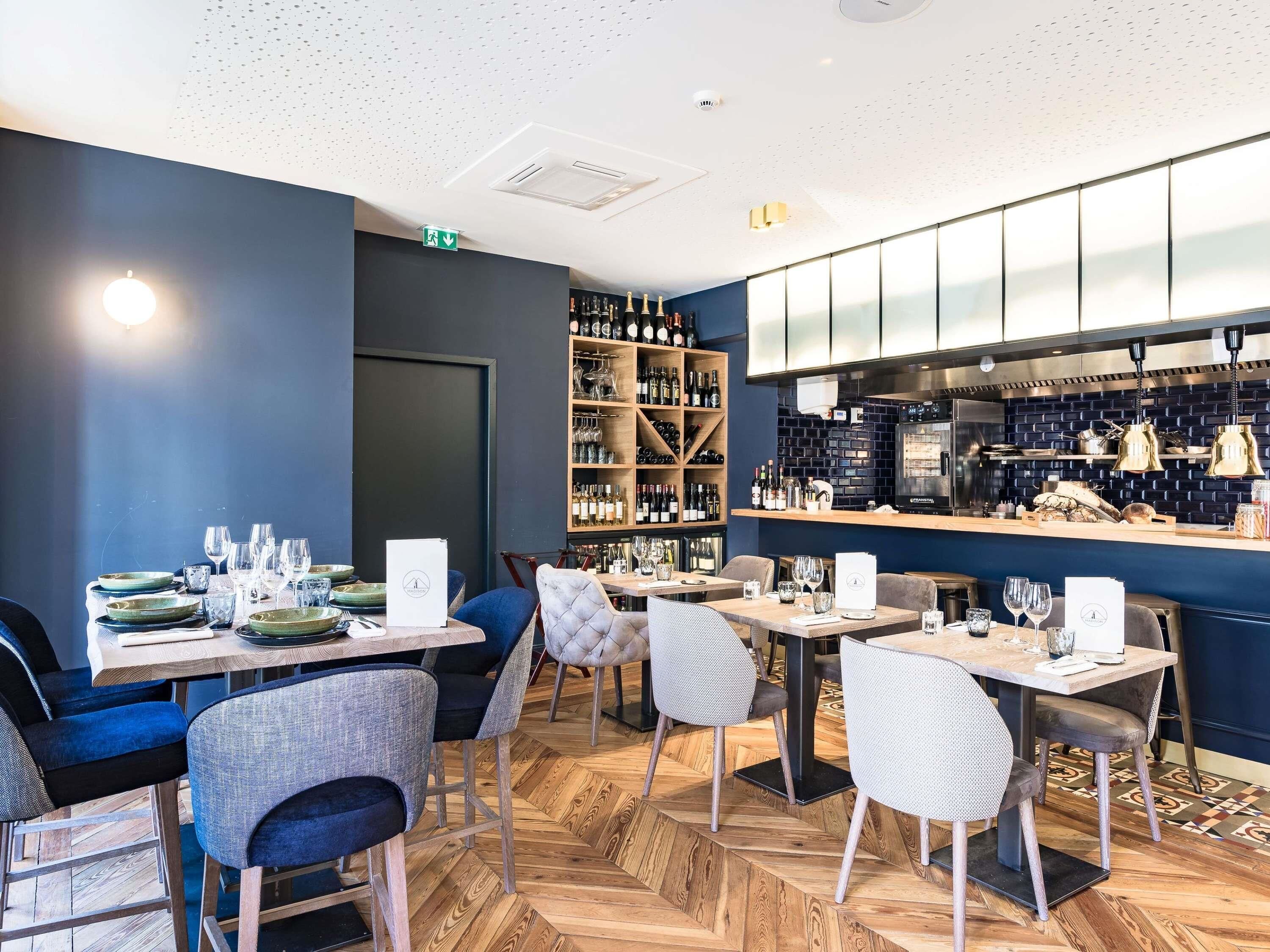 L’intérieur d’un restaurant, avec un plancher en bois, des tables, des chaises, un meuble à vin et un espace cuisine.
