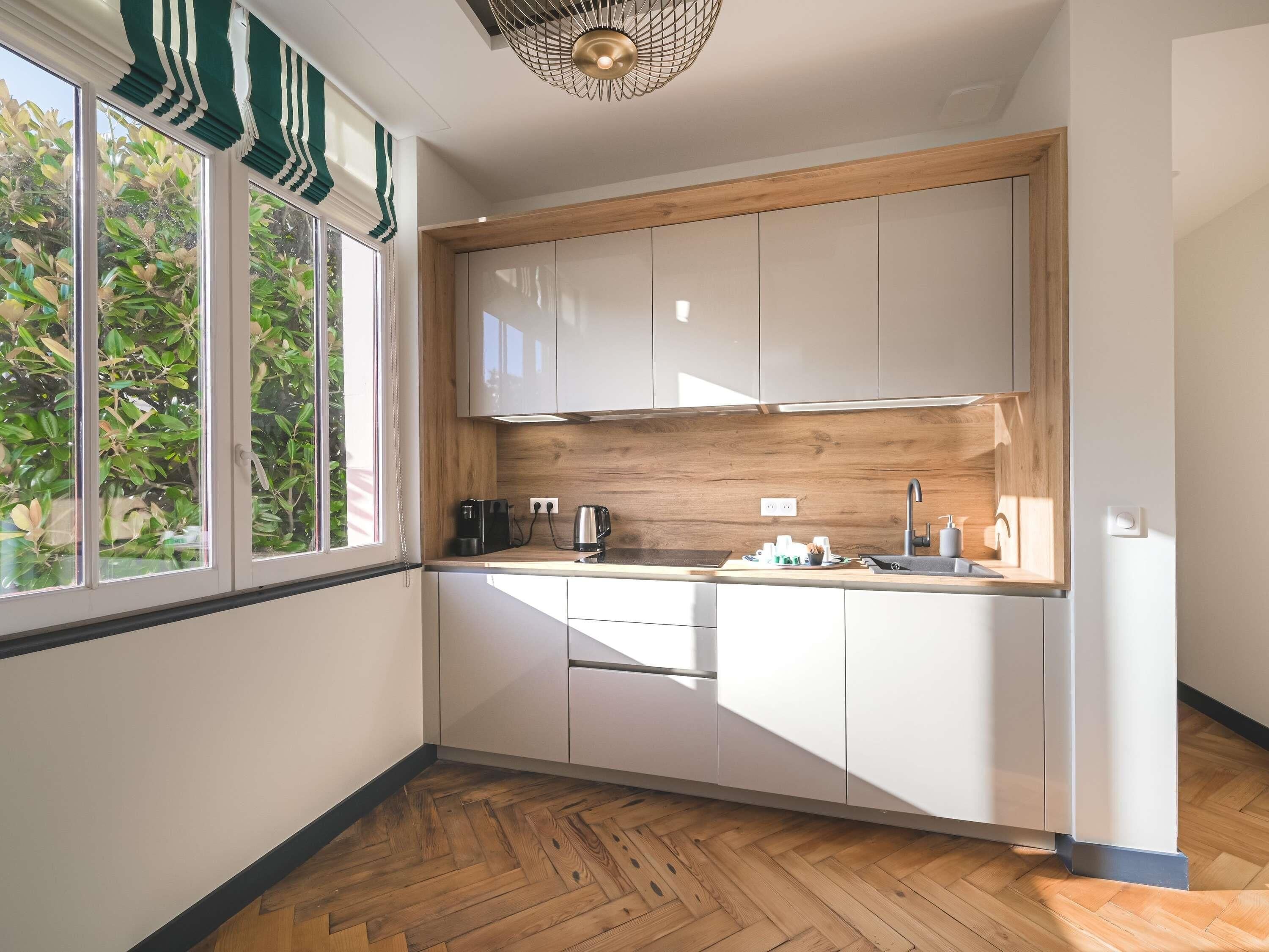 A modern kitchen with white cabinets, a wooden countertop, and a window with green curtains.