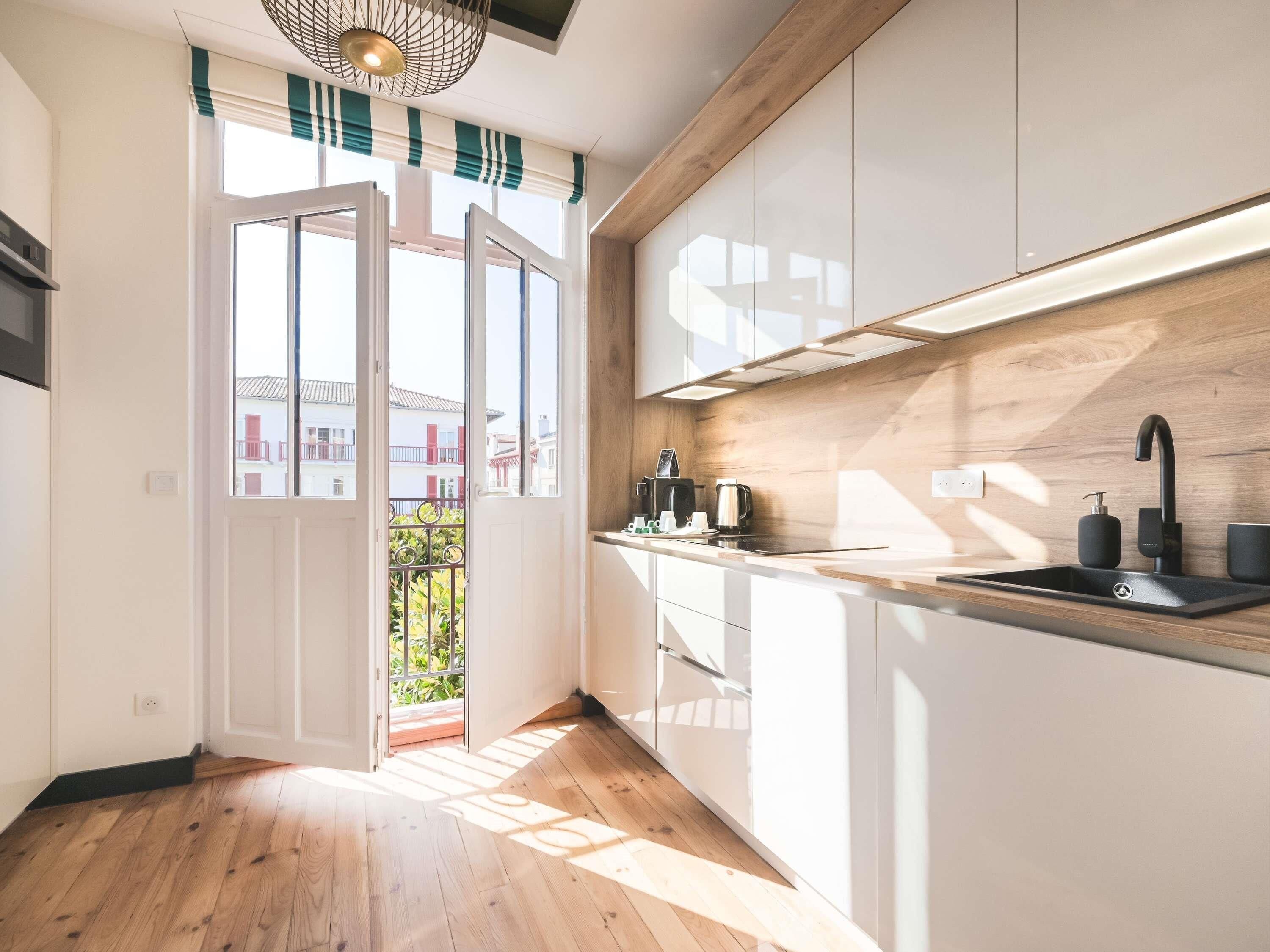 A modern kitchen with wooden flooring, white cabinets, a black sink, and a view of the outside.
