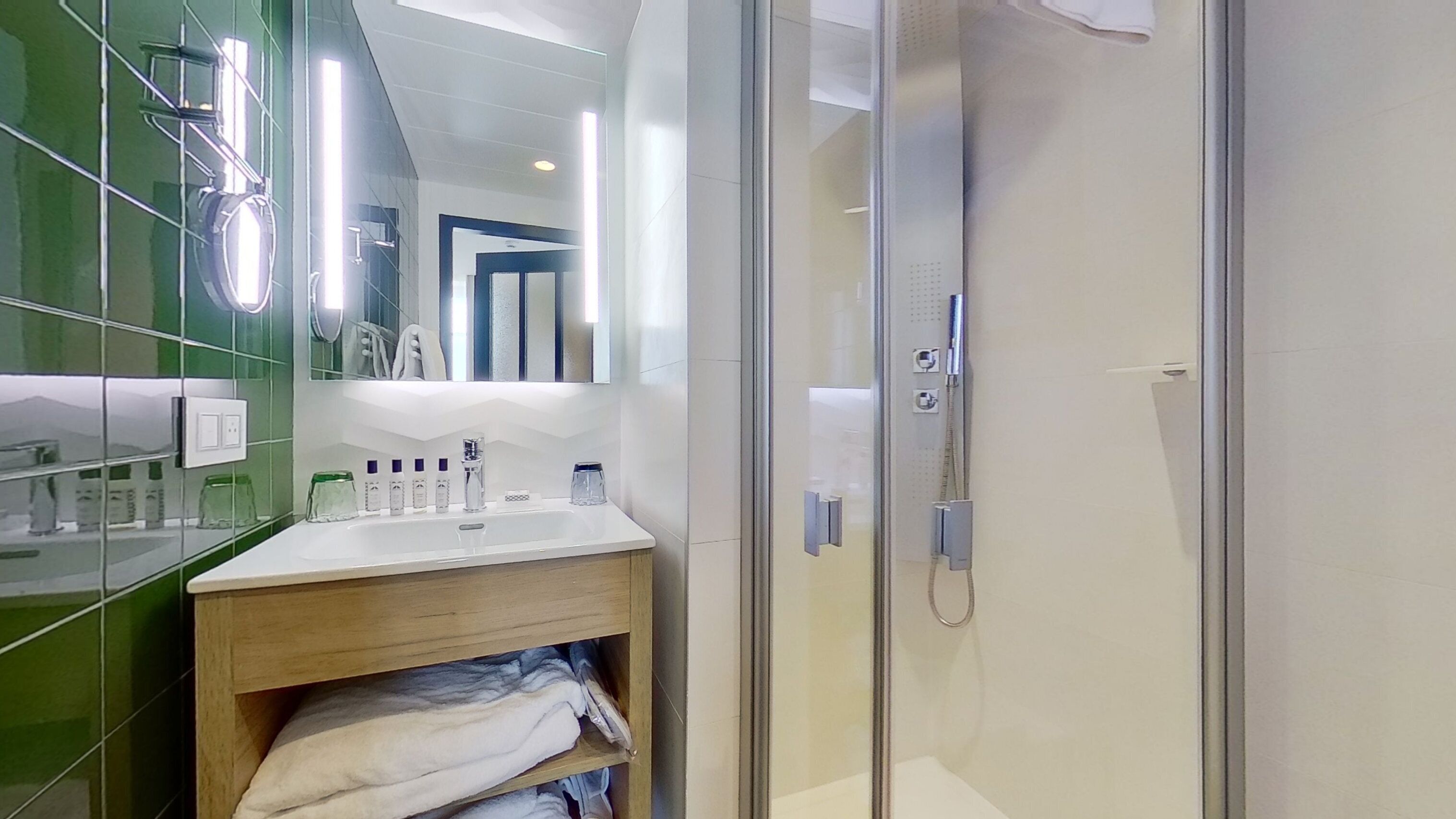 Une salle de bain moderne avec une douche à l’italienne en verre, un lavabo blanc avec un meuble-vasque en bois, et un miroir au-dessus du lavabo.