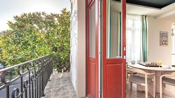 Un balcon avec une balustrade en métal, une porte rouge et une vue sur un arbre verdoyant.