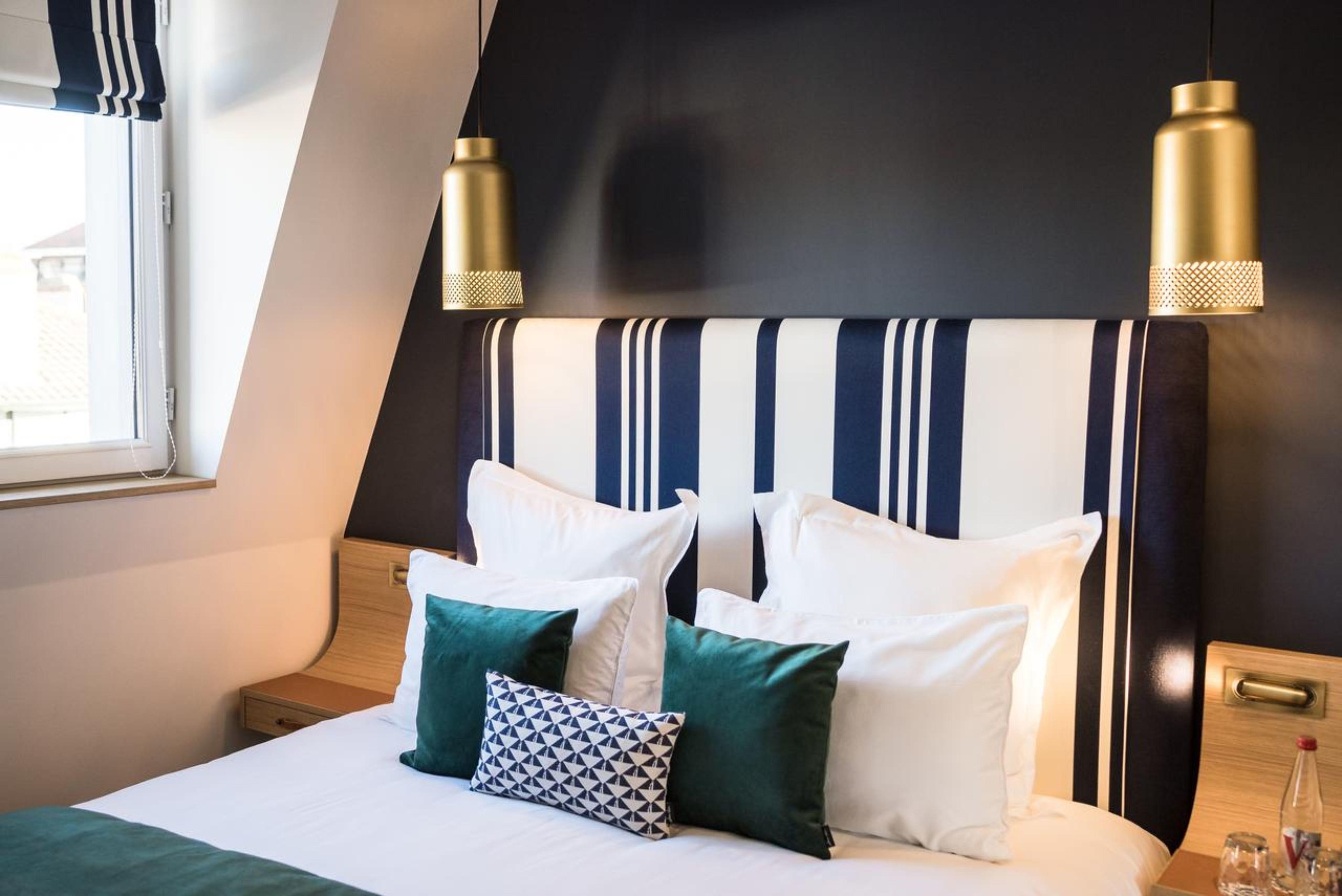 A neatly made bed with white and green pillows, a striped headboard, and two pendant lights.