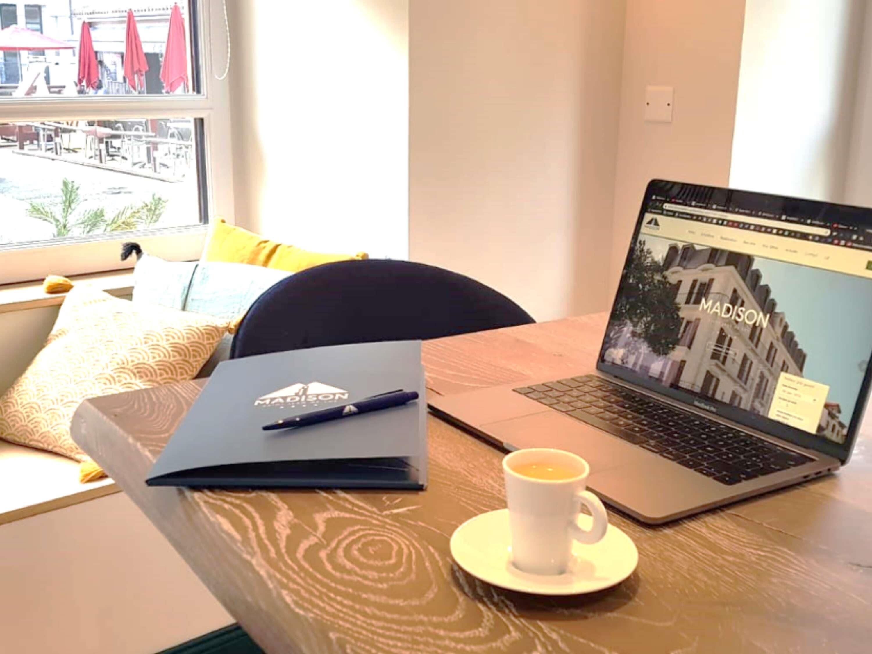A laptop on a table with a cup of coffee, a notebook, and a pen.