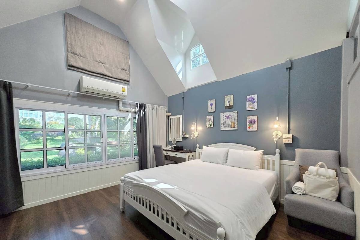 A bedroom with a large bed, a desk, a chair, and a view of the outdoors.