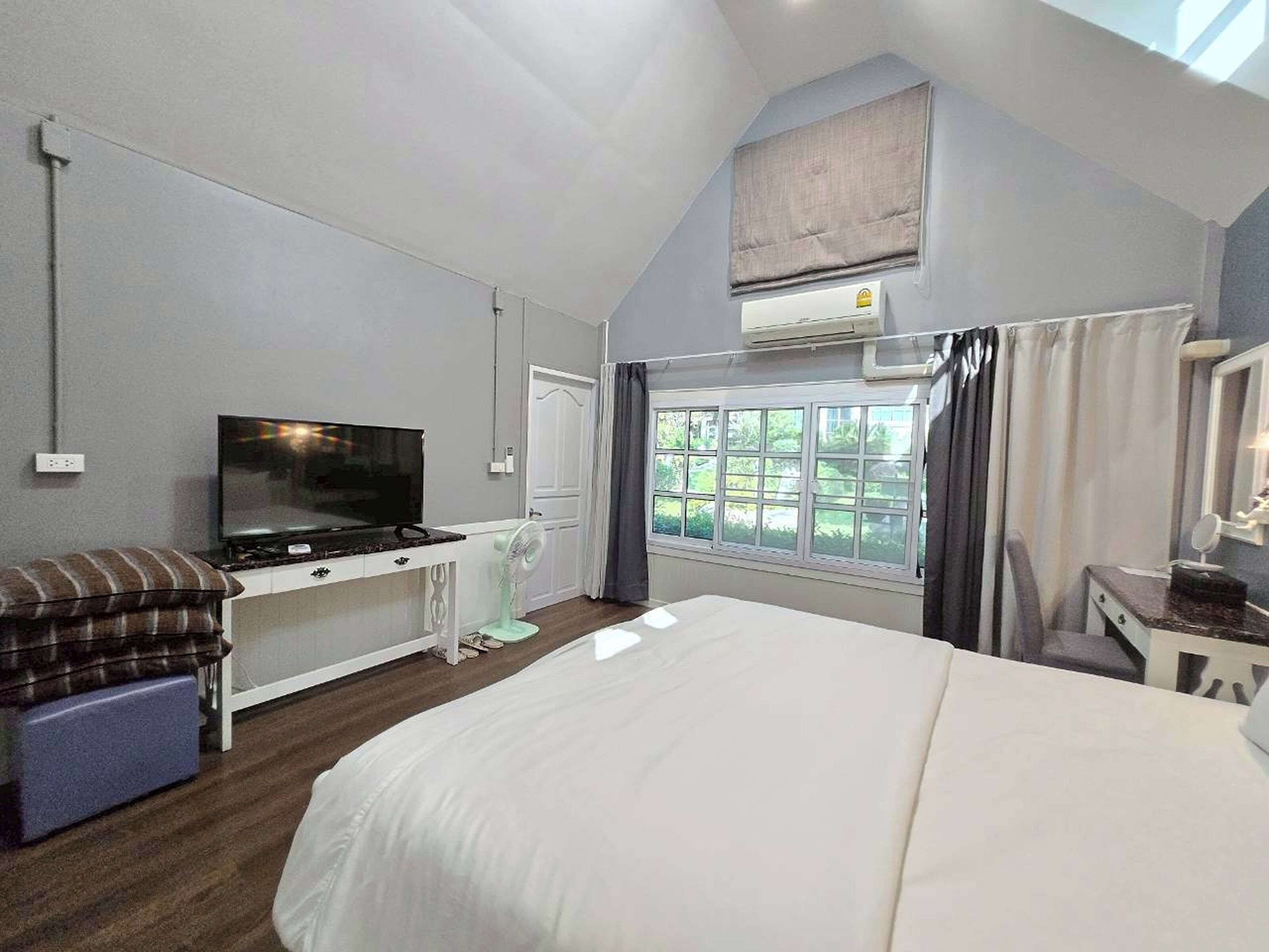 Un dormitorio con cama, televisor, escritorio y ventana con cortinas.