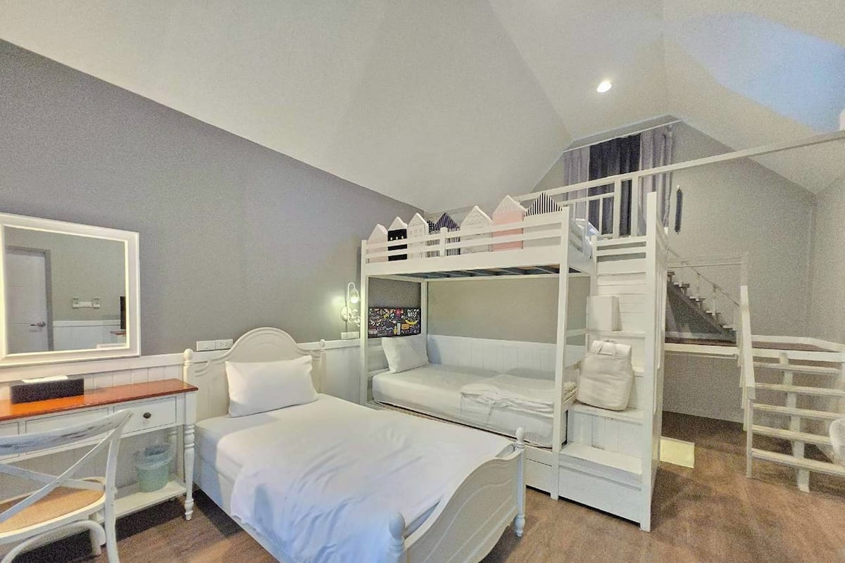 A bunk bed room with a desk and chair, a mirror, and a staircase.