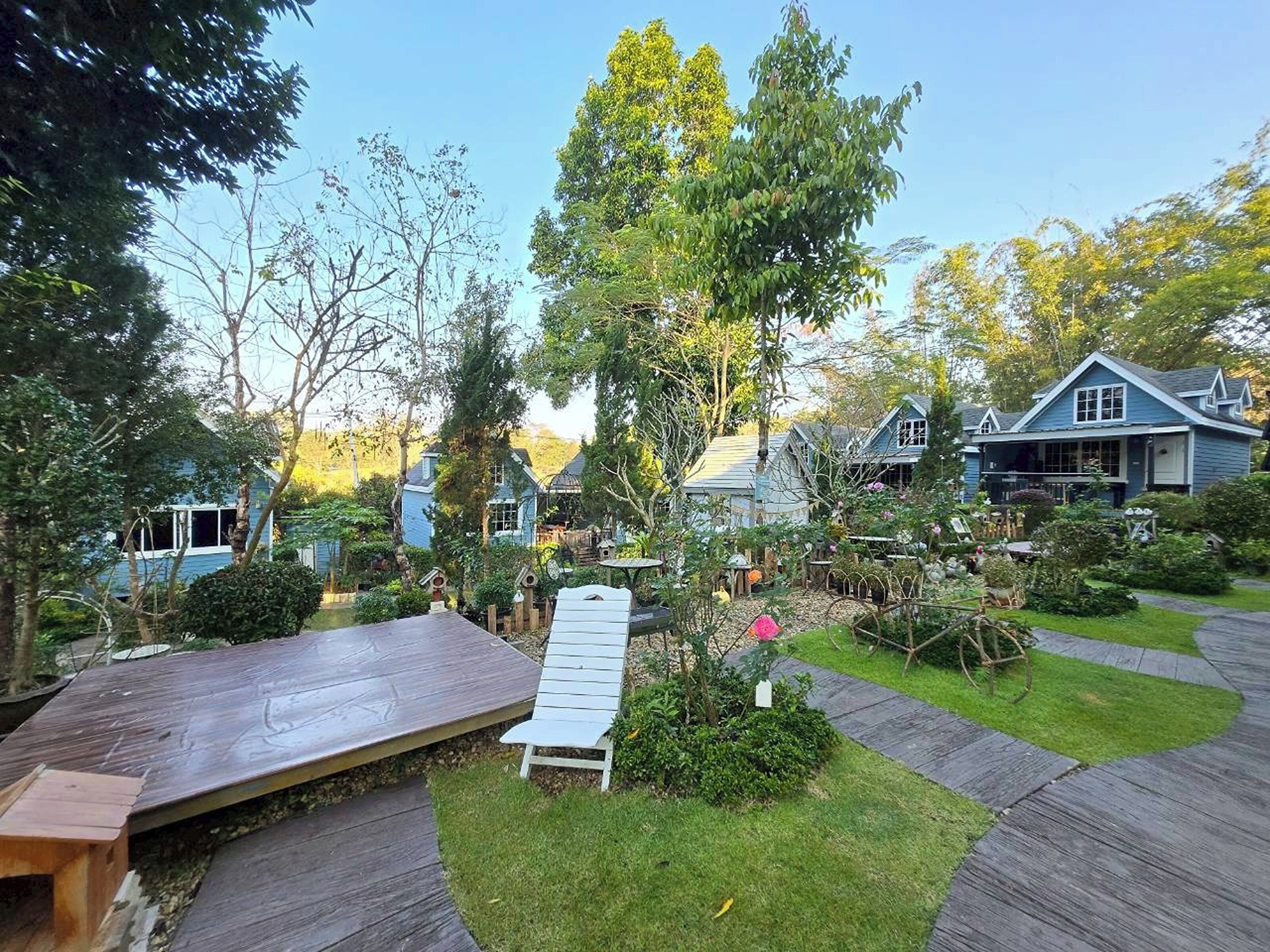 Un espace résidentiel doté d’une terrasse en bois, d’un banc et d’un jardin où l’on trouve diverses plantes ainsi qu’un nichoir.