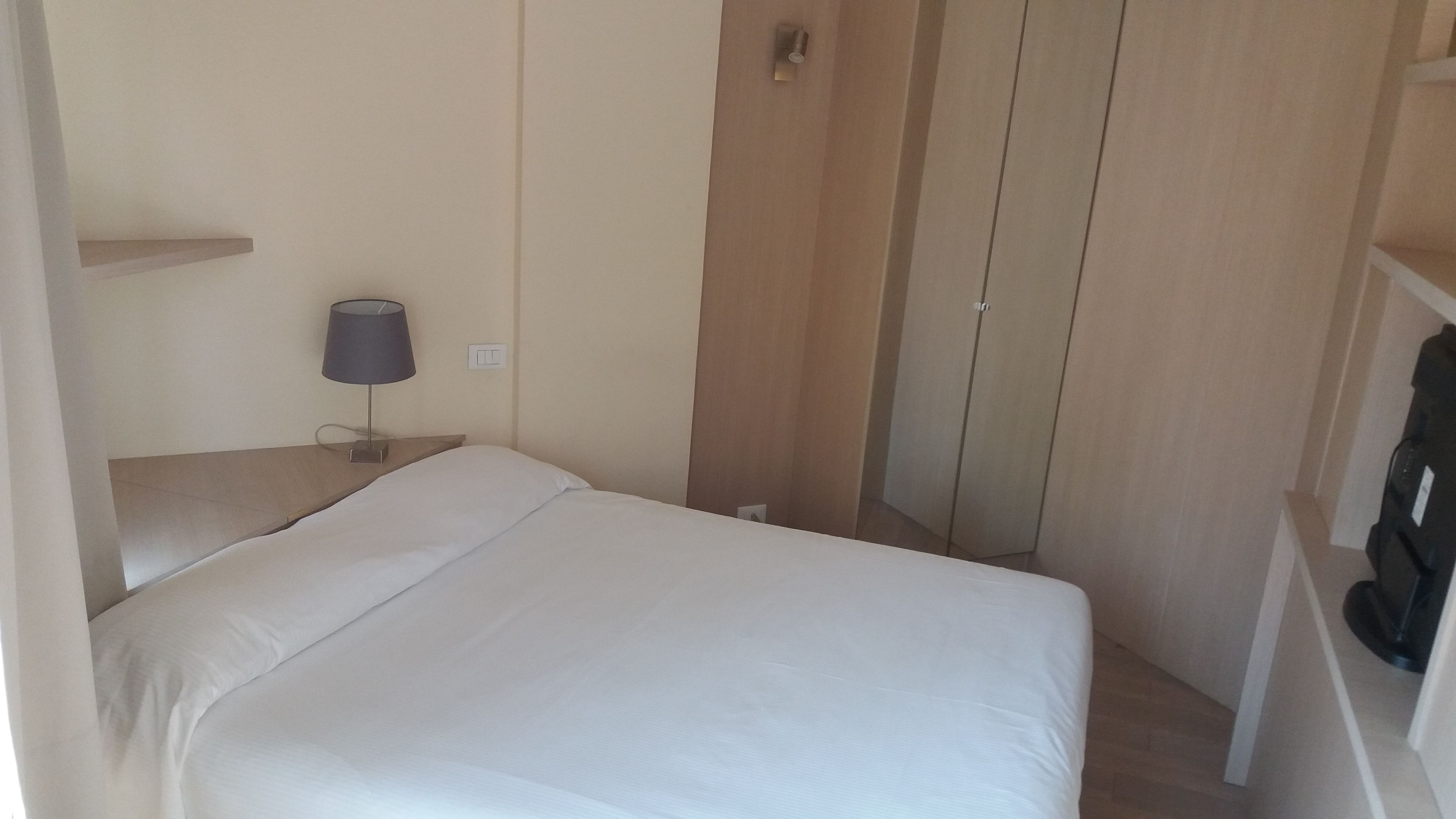 Un dormitorio pequeño y ordenado con cama, mesita de noche, lámpara y armario.
