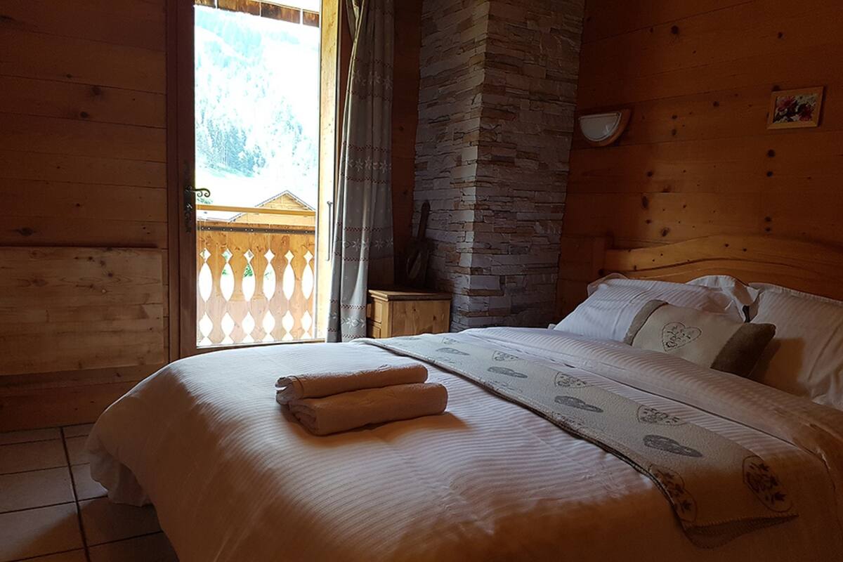 Quarto de cabana de madeira com cama, mesa de cabeceira e parede de pedra.