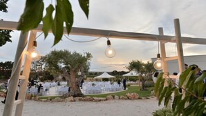 An outdoor event with round tables and chairs, string lights, and a wooden pergola. - Masseria Corte Masseriola (Alberobello)