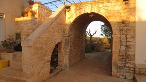A stone archway leading to a courtyard with a staircase on the left and a potted plant on the right. - Masseria Corte Masseriola (Alberobello)