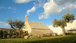 A stone building with a sloped roof, surrounded by grass and trees. - Masseria Corte Masseriola (Alberobello)