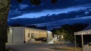 An outdoor venue with a covered seating area and a tent, surrounded by trees and a building with a white facade. - Masseria Corte Masseriola (Alberobello)