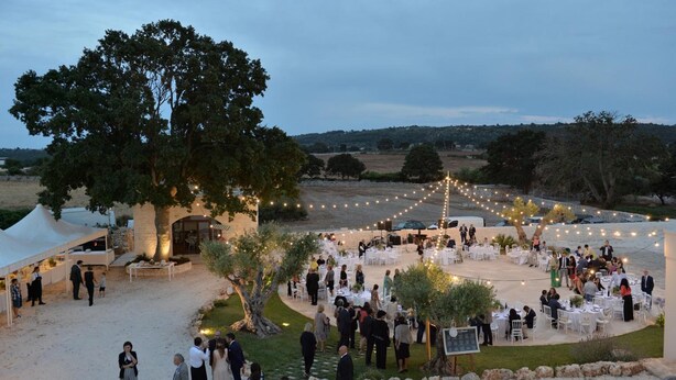 An outdoor event with tables and chairs arranged under a large tree, surrounded by string lights. - Masseria Corte Masseriola (Alberobello)