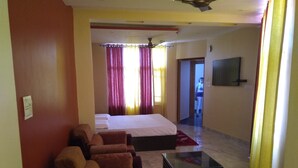 Una habitación de hotel con cama, sofá, mesa de centro y televisor en la pared.