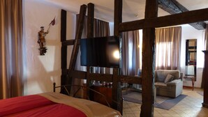 Een kamer met een bed, een televisie, een bank en een houten plafondconstructie.