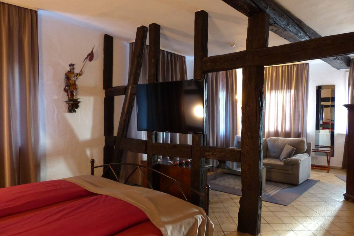 A room with a bed, a television, a sofa, and a wooden ceiling structure.