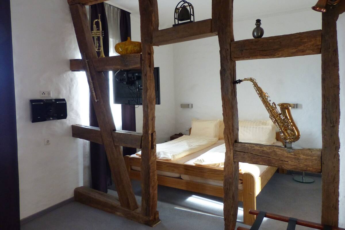 A room with a wooden bed frame, a saxophone, a television, and a small table with a vase.