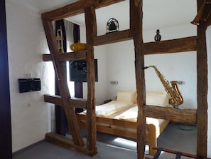 Une chambre avec un lit en bois, un saxophone, une télévision et une petite table sur laquelle se trouve un vase.