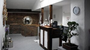 Een receptiezone met een houten balie, een potplant, een klok aan de muur en een trap naar een lager gelegen niveau.