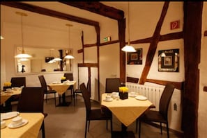 Un espace repas avec des tables préparées pour deux personnes, des poutres en bois au plafond et des luminaires suspendus.