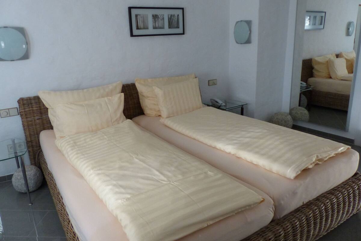 A double bed with two pillows, a bedside table with a phone, and a mirror on the wall.