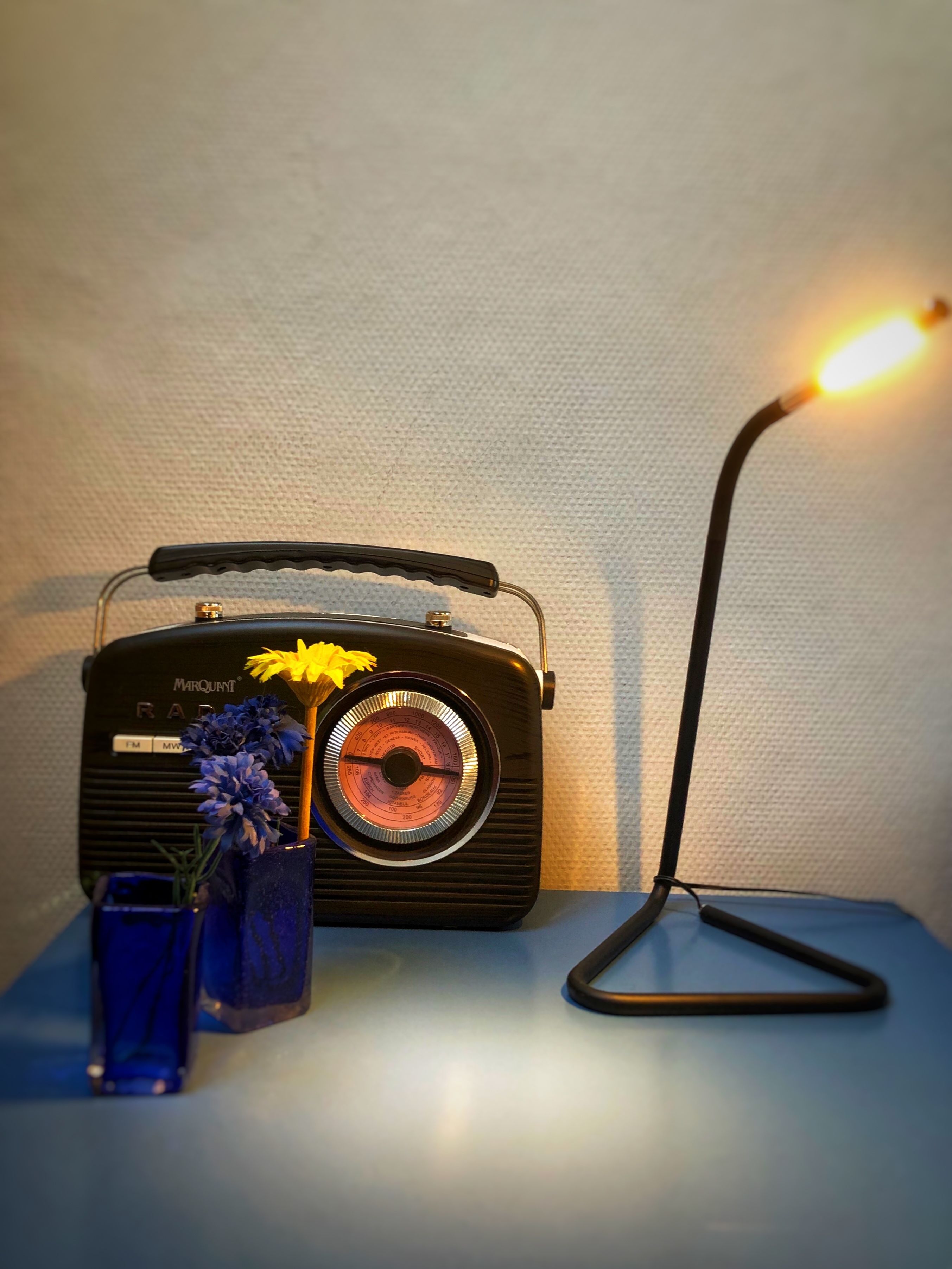 A vintage Marquardt radio on a table with a vase of flowers and a lamp.