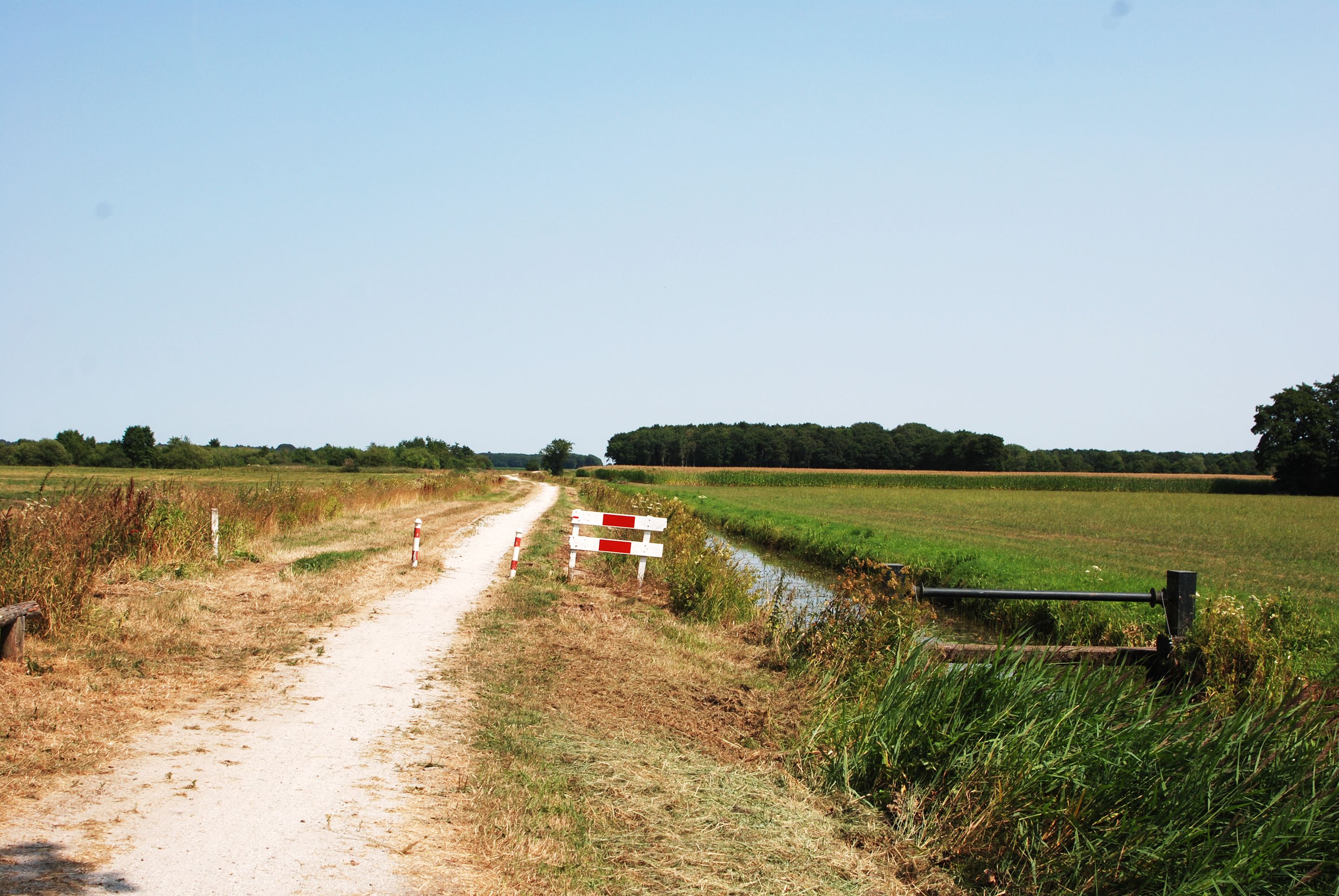 Un camino rural de tierra con una barrera roja y blanca y un canal de agua a la derecha.