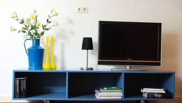 Een blauwe entertainmentkast met een flatscreen televisie, een vaas met bloemen, een lamp en boeken.