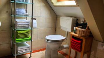 A bathroom with a toilet, a glass shelf with towels, a basket, and a skylight.
