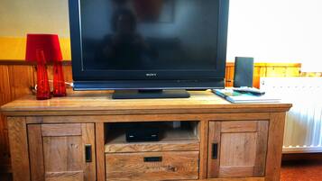 Een Sony televisie op een houten tv-meubel, met een rode lamp, een boek en een afstandsbediening.