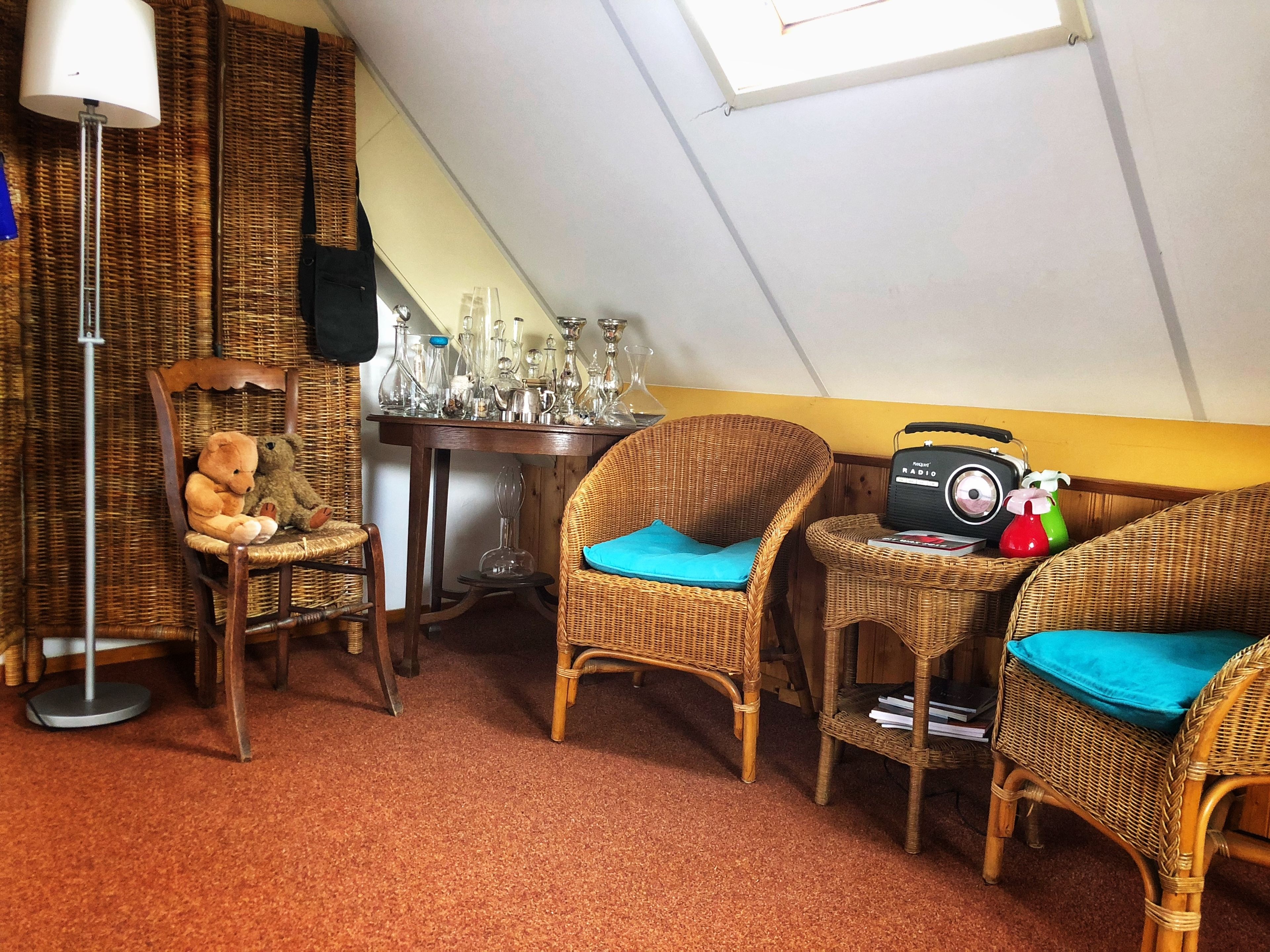 A cozy attic room with wicker furniture, a table with glassware, and a radio.