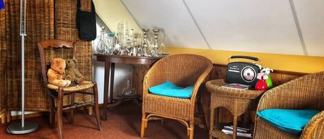 A cozy attic room with wicker furniture, a table with glassware, and a radio.