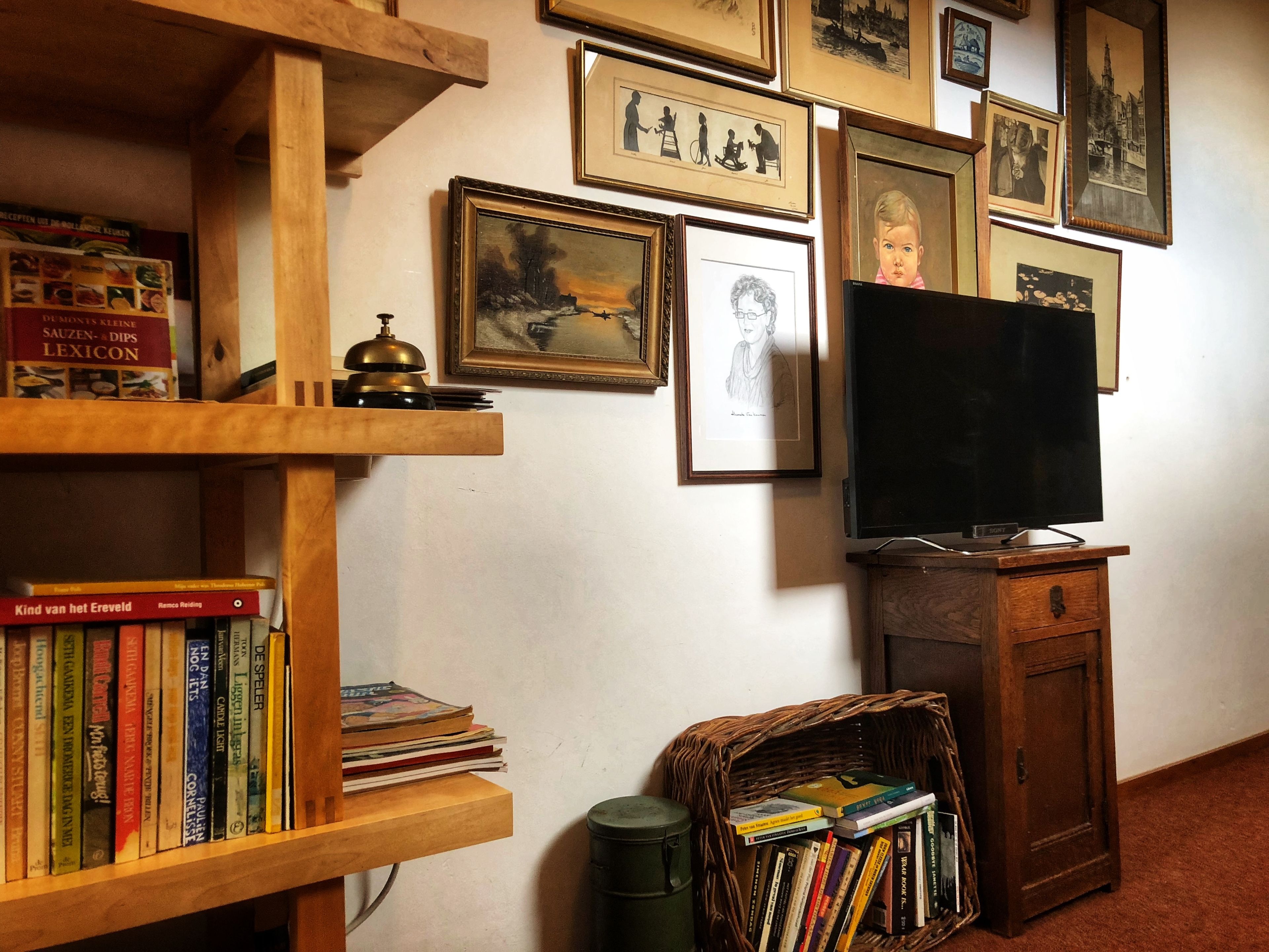 A room with a wooden bookshelf filled with books, a television on a wooden stand, and framed pictures on the wall.